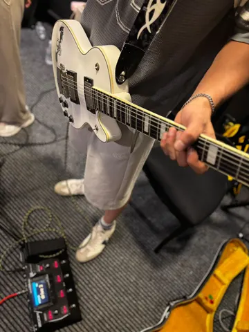 Pedalboard başında beyaz elektro gitarla çalan müzisyen